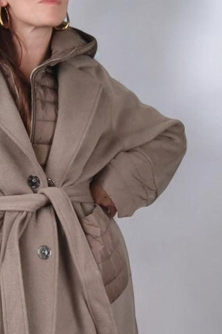 Cappotto lungo con collo classico a revers, chiusura con bottoni automatici e cintura in vita. Dotato di un'imbottitura interna staccabile, che può essere utilizzata separatamente come gilet con cappuccio. Presenta tasche e polsini realizzati nello stesso tessuto imbottito del gilet, rendendolo un capo versatile e adatto a diverse temperature.