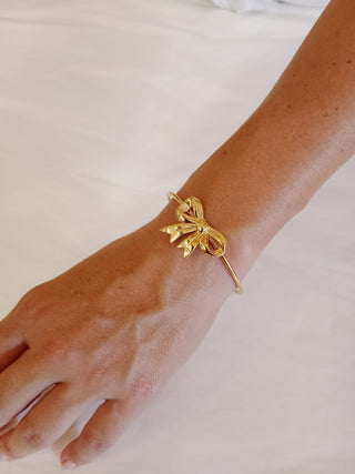 Braccio che indossa bracciale rigido con fiocco colore oro