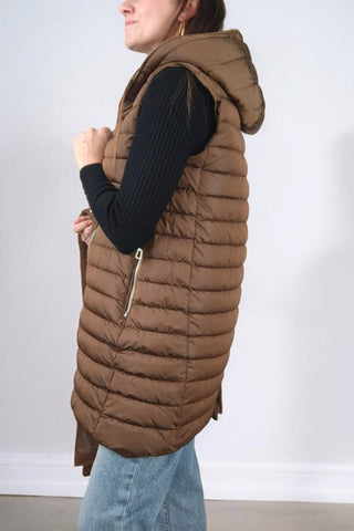 Cappotto lungo con collo classico a revers, chiusura con bottoni automatici e cintura in vita. Dotato di un'imbottitura interna staccabile, che può essere utilizzata separatamente come gilet con cappuccio. Presenta tasche e polsini realizzati nello stesso tessuto imbottito del gilet, rendendolo un capo versatile e adatto a diverse temperature.