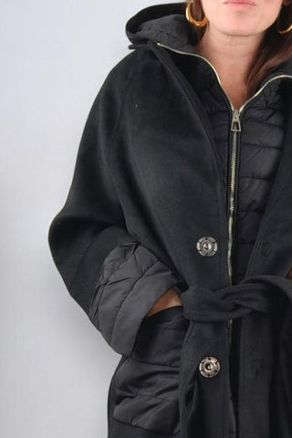 Cappotto lungo con collo classico a revers, chiusura con bottoni automatici e cintura in vita. Dotato di un'imbottitura interna staccabile, che può essere utilizzata separatamente come gilet con cappuccio. Presenta tasche e polsini realizzati nello stesso tessuto imbottito del gilet, rendendolo un capo versatile e adatto a diverse temperature.