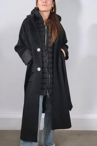 Cappotto lungo con collo classico a revers, chiusura con bottoni automatici e cintura in vita. Dotato di un'imbottitura interna staccabile, che può essere utilizzata separatamente come gilet con cappuccio. Presenta tasche e polsini realizzati nello stesso tessuto imbottito del gilet, rendendolo un capo versatile e adatto a diverse temperature.